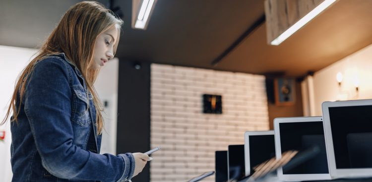 young attractive girl in electronics store stands at desk and tests phone. phones shop. concept of buying gadgets.