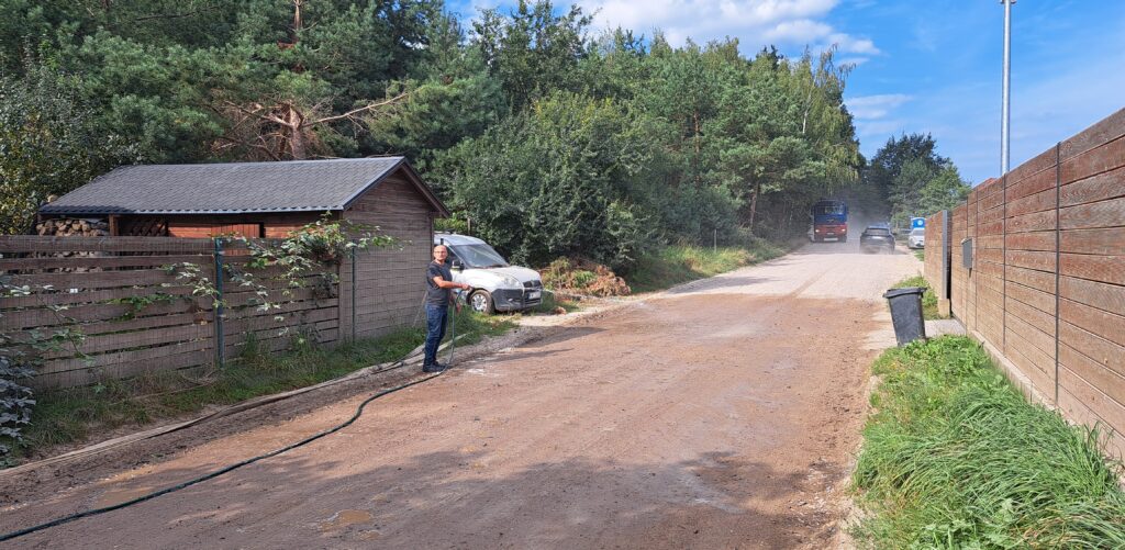 Jeden z mieszkańców polewa drogę wodą z węża ogrodowego, żeby zminimalizować uciążliwości