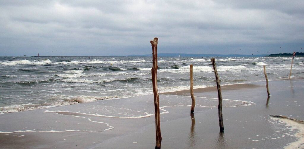 Morski brzeg, kije wbite w piach, fale