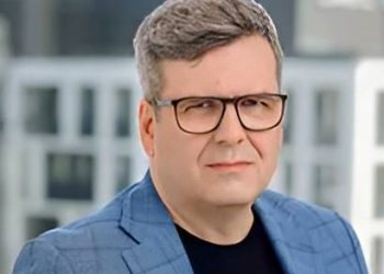 Wojciech Rynkowski, ekspert portalu Extradom.pl, w okularach i niebieskiej marynarce w kratę na jasnym tle. Gość Radia Gdańsk opowiadał o koszcie budowy domów