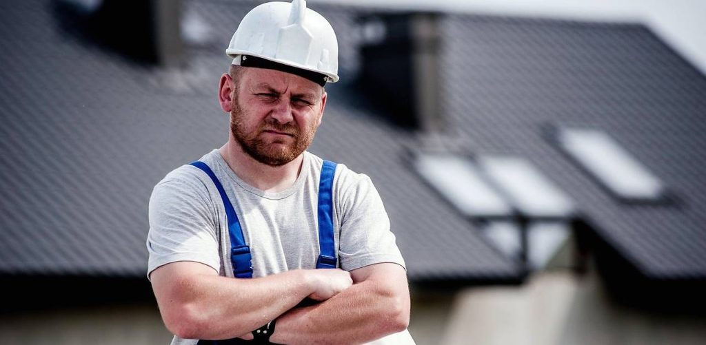 Pracownik budowlany w kasku. W tle dach budynku