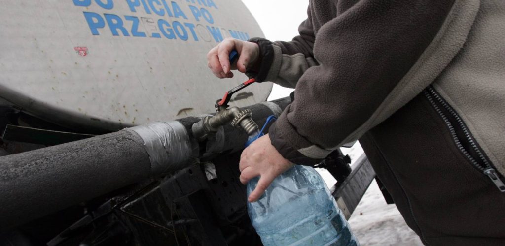 Beczkowóz. Osoba nabiera wody do plastikowej butelki