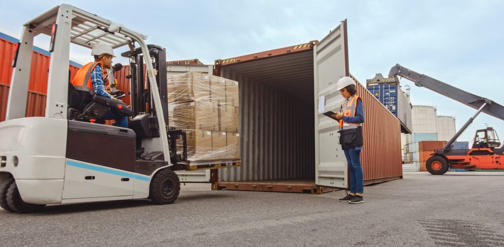 Operator wózka widłowego pod nadzorem inżyniera ładuje paletę z elementami maszyn do kontenera