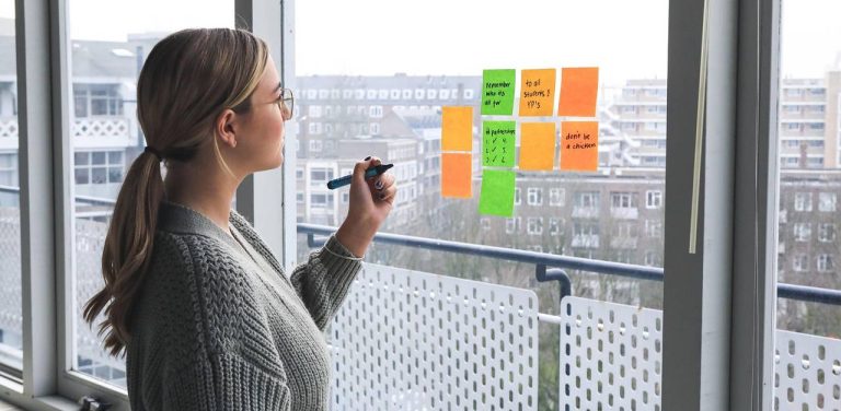 Młoda kobieta w okularach planująca zadania za pomocą kolorowych karteczek samoprzylepnych na szybie okiennej