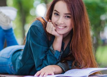 Dziewczyna (studentka) leży na ławce w parku przed nią otwarty zeszyt