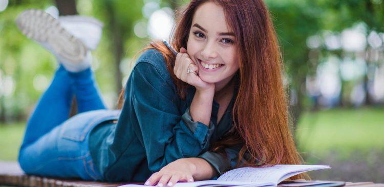 Dziewczyna (studentka) leży na ławce w parku przed nią otwarty zeszyt