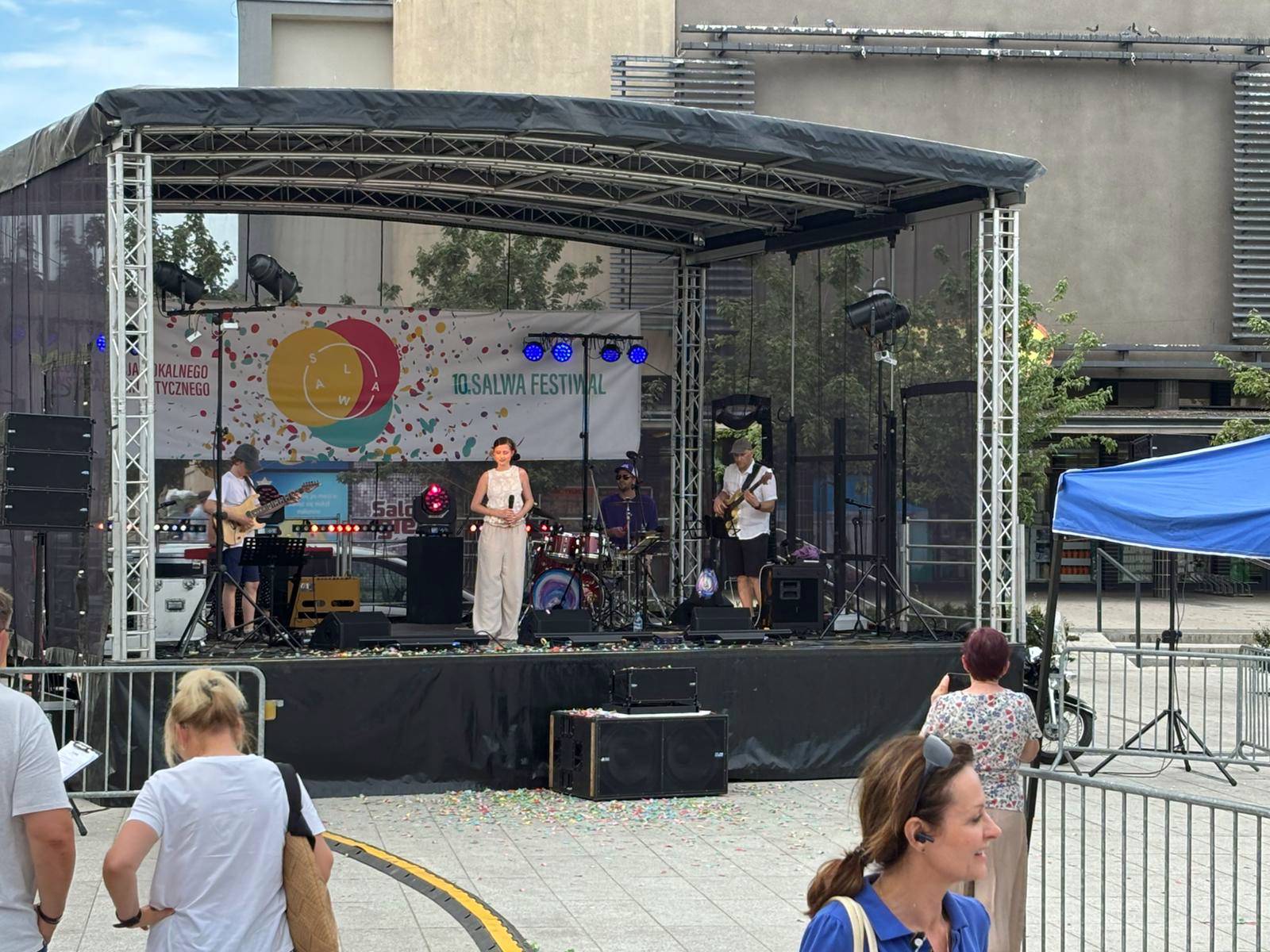 Występ zespołu muzycznego z wokalistką na scenie ozdobionej banerem „10. SALWA FESTIWAL” na Starym Rynku w Słupsku. Przed sceną widoczni są pierwsi widzowie