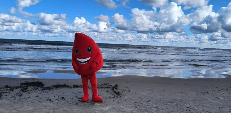 Maskotka krwinki na plaży w Łebie, promująca akcję krwiodawstwa. W tle morze i niebo z niewielkimi chmurami