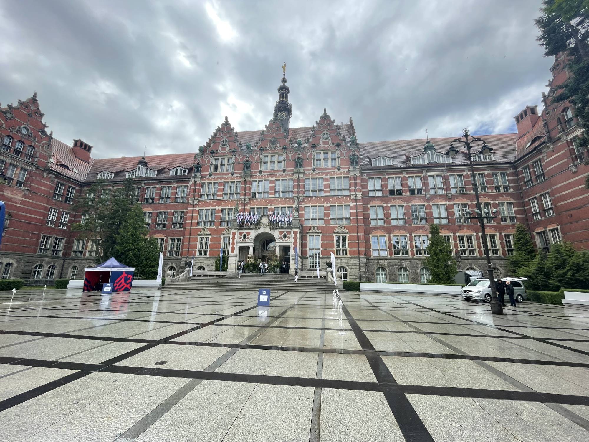 Gmach Główny Politechniki Gdańskiej w pochmurny dzień. Widok na historyczną fasadę budynku i dziedziniec z fontannami. Zabytkowy budynek uczelni w Gdańsku