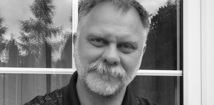 Czarno-białe zdjęcie, Jarosław Pióro stoi na tle okna