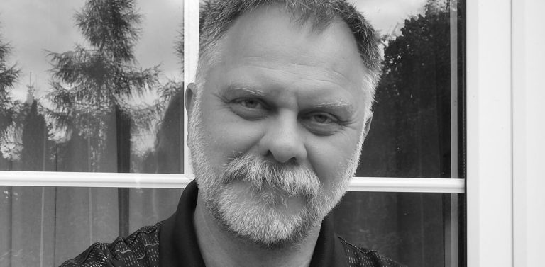 Czarno-białe zdjęcie, Jarosław Pióro stoi na tle okna