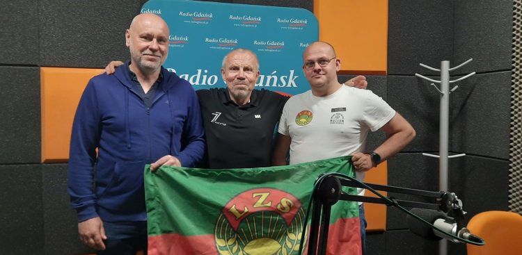 Piotr Klecha, Włodzimierz Machnikowski i Jan Trofimowicz prezentują flagę z logo LZS