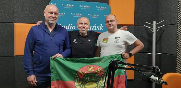Piotr Klecha, Włodzimierz Machnikowski i Jan Trofimowicz prezentują flagę z logo LZS