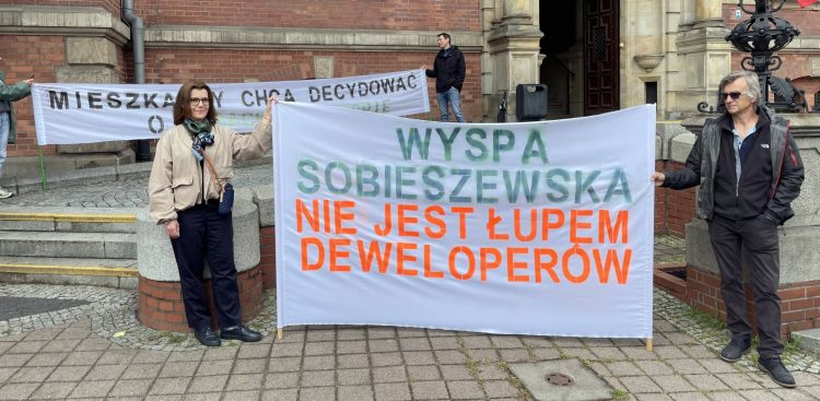 Mieszkańcy Gdańska protestują z transparentem "Wyspa Sobieszewska nie jest łupem deweloperów" przeciwko zabudowie przed budynkiem Rady Miasta Gdańska