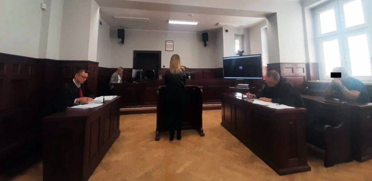 Sala rozpraw Sądu Okręgowego w Słupsku. Przy stołach siedzą prawnicy w togach, na środku tyłem stoi kobieta, a po prawej stronie na ławie siedzi oskarżony kierowca z czarnym paskiem zasłaniającym oczy. Zapada wyrok w sprawie śmiertelnego wypadku w czasie orkanu Ksawery w 2013 roku
