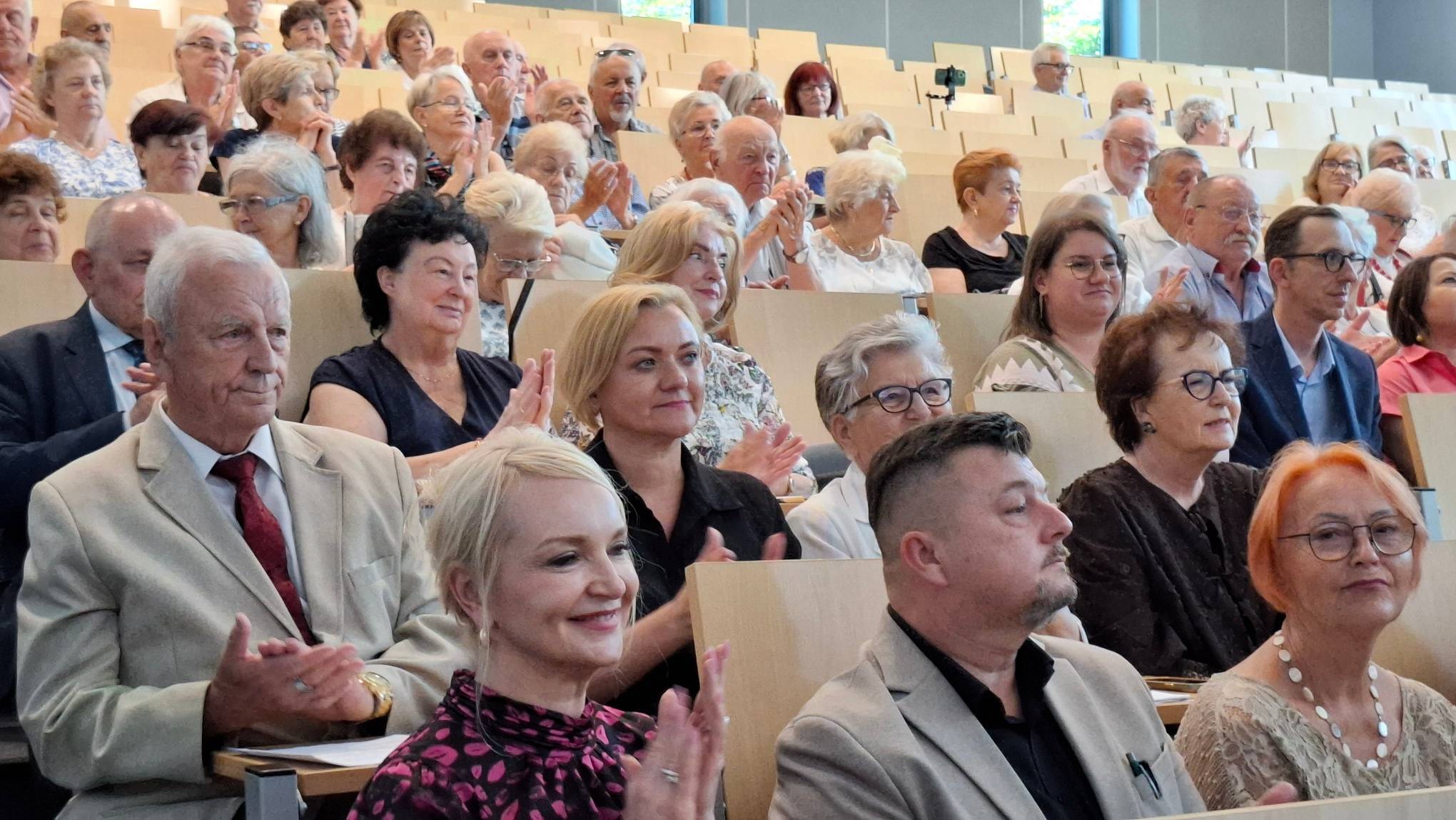 Seniorzy, eksperci i samorządowcy siedzący w amfiteatralnej sali wykładowej Gdańskiej Akademii Medycznej Nauk Stosowanych (GAMNS) i klaszczący podczas debaty o zdrowiu