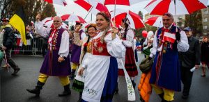 Kobiety i mężczyźni w strojach kaszubskich i z biało-czerwonymi parasolkami. Pochód z okazji gdyńskich obchodów Narodowego Święta Niepodległości w roku 2014