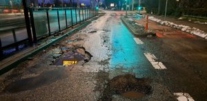 Głębokie wyrwy i dziury z kałużami wody na mocno zniszczonej jezdni ulicy Wita Stwosza w Gdańsku, tuż obok przystanku tramwajowego po zmroku. Ul. Wita Stwosza w Gdańsku-Oliwie doczeka się odnowy nawierzchni