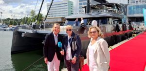 Anna Rębas stoi na czerwonym dywanie przed jachtem w towarzystwie dwóch kobiet. Zdjęcie wykonane podczas siódmej edycji Polboat Yachting Festival, największej w Polsce wystawy jachtów na wodzie.