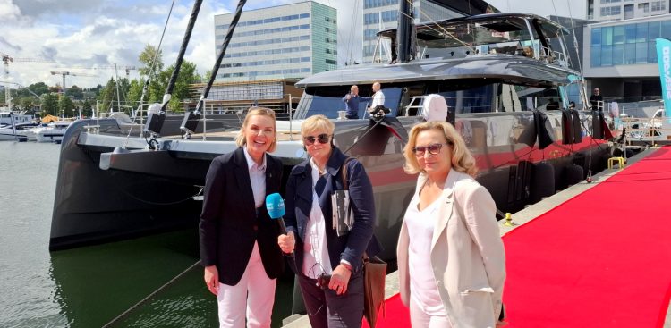 Anna Rębas stoi na czerwonym dywanie przed jachtem w towarzystwie dwóch kobiet. Zdjęcie wykonane podczas siódmej edycji Polboat Yachting Festival, największej w Polsce wystawy jachtów na wodzie.