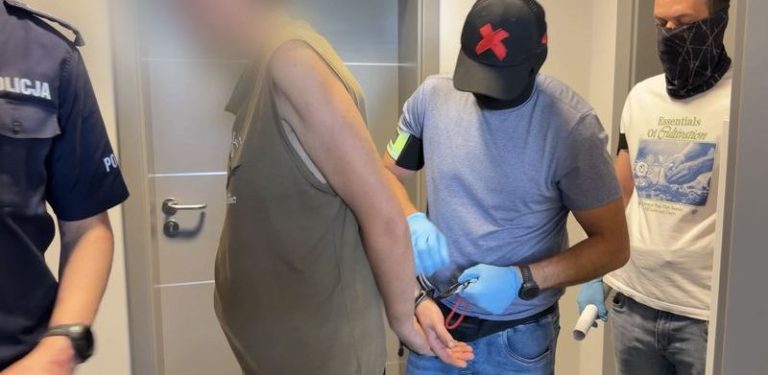 Policjanci w rękawiczkach ochronnych i mężczyzna w kajdankach z zamazaną twarzą, ubrany w bezrękawnik. Po lewej stronie stoi umundurowany policjant, a po prawej drugi cywilny funkcjonariusz z zasłoniętą twarzą. Zatrzymany zaatakował w Rumi nożem innego mężczyznę na tle narodowościowym