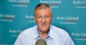 Adam Liszczewski, przewodniczący Rady OPZZ Województwa Pomorskiego, w jasnoniebieskiej koszuli siedzi przed mikrofonem na tle niebiesko-turkusowej ścianki z powtarzającym się logo Radia Gdańsk