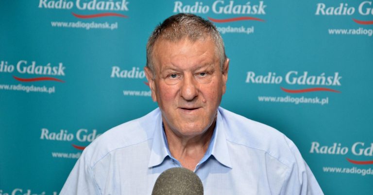 Adam Liszczewski, przewodniczący Rady OPZZ Województwa Pomorskiego, w jasnoniebieskiej koszuli siedzi przed mikrofonem na tle niebiesko-turkusowej ścianki z powtarzającym się logo Radia Gdańsk