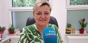 Dr Dagmara Wiewiórkowska-Garczewska uśmiecha się przed niebieskim mikrofonem z logo Radia Gdańsk w czasie nagrania najnowszej audycji, w której mówi, co i jak często pić w czasie upałów, żeby się nie odwodnić