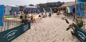 Farma Dobrej Energii na plaży w Ustce. Drewniane podesty, leżaki, pufy i zadaszone stoiska informacyjne Fundacji PGE w strefie „Farma Dobrej Energii” na plaży w Ustce, wokół której wypoczywają dorośli i dzieci
