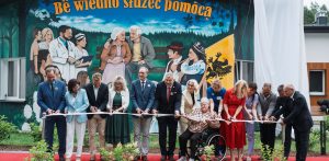 Otwarcie Kaszubskiego Centrum Senioralnego w Dzierżążnie. Grupa samorządowców, medyków oraz seniorów stoi przed kolorowym budynkiem i trzyma wstęgę, która przecinana jest przez kilka osób jednocześnie