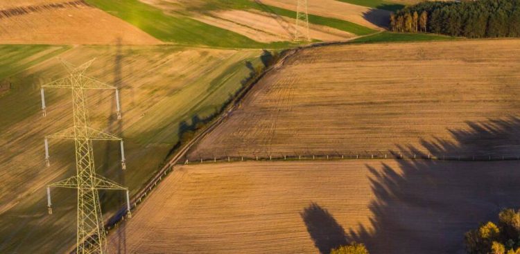 Wysoki, stalowy słup elektroenergetyczny linii najwyższych napięć 400 kV na tle błękitnego nieba i zielonych pól na Pomorzu