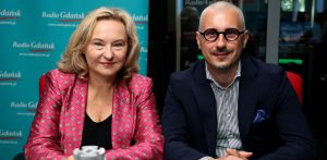 Kobieta o jasnych, blond włosach w różowym żakiecie we wzory oraz mężczyzna w okularach, pasiastej koszuli i ciemnej marynarce. Oboje siedzą uśmiechnięci przy stole w studiu na tle turkusowej ścianki z logo Radia Gdańsk. To Marta Chełkowska i Tomasz Smorgowicz w studiu Radia Gdańsk