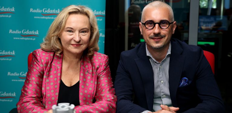 Kobieta o jasnych, blond włosach w różowym żakiecie we wzory oraz mężczyzna w okularach, pasiastej koszuli i ciemnej marynarce. Oboje siedzą uśmiechnięci przy stole w studiu na tle turkusowej ścianki z logo Radia Gdańsk. To Marta Chełkowska i Tomasz Smorgowicz w studiu Radia Gdańsk