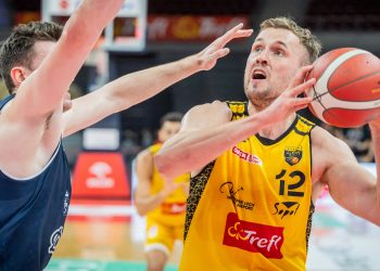 Koszykarz Mikołaj Witliński w żółto-czarnym stroju Energi Trefla Sopot z numerem 12 trzyma oburącz piłkę podczas meczu, próbując minąć blokującego go zawodnika w granatowym stroju drużyny Dziki Warszawa