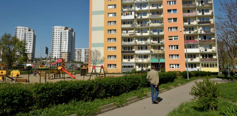 Blok na ulicy Warneńskiej w dzielnicy Piecki-Migowo w Gdańsku. Na pierwszym planie mężczyzna spacerujący po chodniku. Po prawej widoczny jest plac zabaw.