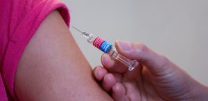 Zbliżenie na ramię dziecka, któremu osoba w niebieskich rękawiczkach jednorazowych podaje szczepionkę za pomocą strzykawki. Jak podaje Wojewódzka Stacja Sanitarno-Epidemiologiczna w Gdańsku, na pomorzu rośnie liczba niezaszczepionych dzieci