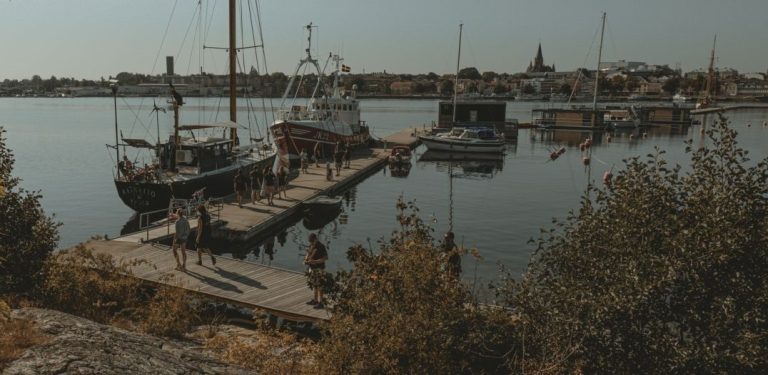 Nz. statek przy pomoście i zmierzający do niego ludzie