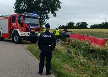 Na skraju drogi stoi tyłem policjant obserwujący miejsce wypadku na drodze powiatowej między Sztumem a Postolinem, w którym zginęły cztery osoby. Po lewej stronie zaparkowany jest czerwony wóz strażacki z włączonymi sygnałami świetlnymi, a po prawej – w rowie obok pola zboża – strażacy rozwijają czerwony parawan, który zasłania przewrócony na dach, zniszczony samochód osobowy. W sprawie wypadku wszczęto śledztwo