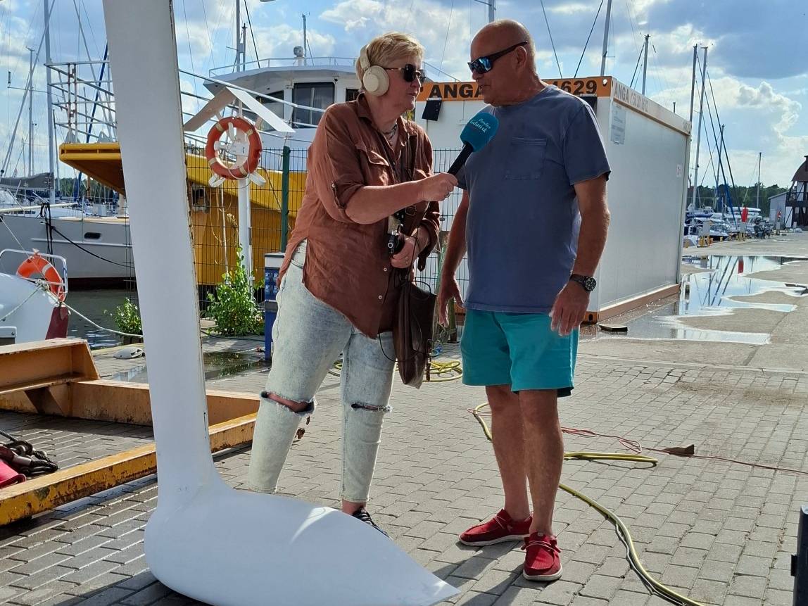 Dziennikarka radiowa Anna Rębas przeprowadza wywiad z kapitanem Romanem Paszke w marinie na tle jachtów przed rozpoczęciem regat PGE Baltica Race
