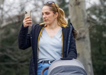 Kobieta z wózkiem dziecięcym w parku bezskutecznie szuka sygnału w telefonie w gminie Lipnica. Zdjęcie ilustracyjne