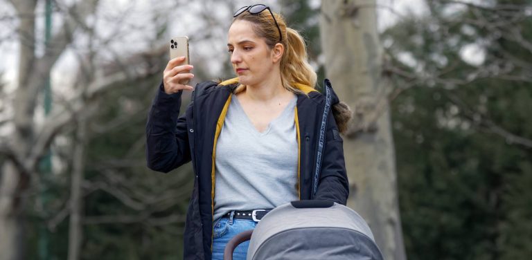 Kobieta z wózkiem dziecięcym w parku bezskutecznie szuka sygnału w telefonie w gminie Lipnica. Zdjęcie ilustracyjne