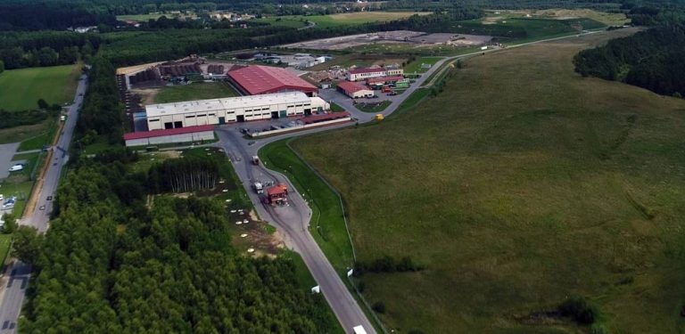 Widok z lotu ptaka na kompleks zakładu zagospodarowania odpadów Eko Dolina w Łężycach, hale magazynowe, bramę wjazdową oraz otaczające je zielone wzgórza i lasy. Eko Dolina zapowiada powstanie nowego PSZOK-u dla mieszkańców Gdyni, Rumi i Wejherowa