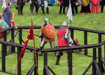 Festiwal Rycerski w Sztumie. Dwaj rycerze w pełnych zbrojach płytowych walczą na trawie w drewnianej arenie, otoczeni przez widzów i rekonstruktorów w średniowiecznych strojach