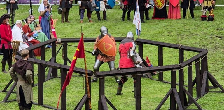 Festiwal Rycerski w Sztumie. Dwaj rycerze w pełnych zbrojach płytowych walczą na trawie w drewnianej arenie, otoczeni przez widzów i rekonstruktorów w średniowiecznych strojach