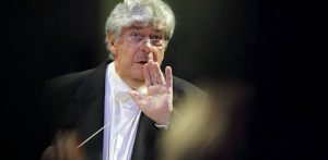 Dyrygent Jan Łukaszewski we fraku i okularach, trzymający batutę i wykonujący gest otwartą dłonią