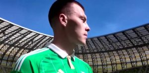 Kacper Łopata w zielonej koszulce Lechii Gdańsk z biało-zielonym kołnierzykiem, stojący na tle trybun stadionu Polsat Plus Arena Gdańsk.
