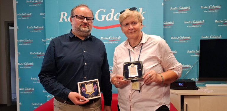 Kapitan Michał Sadowski i Anna Rębas z Radia Gdańsk na tle ściany z logo Radia Gdańsk. Kapitan udzielił dziennikarce pierwszego wywiadu po powrocie z rejsu Darem Młodzieży do USA