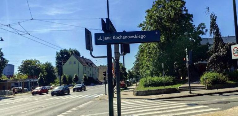 Skrzyżowanie Al. Niepodległości z ul. Jana Kochanowskiego w Sopocie. Na pierwszym planie widoczny jest słupek ze znakiem "ul. Jana Kochanowskiego", w tle wielopasmowa jezdnia z jadącymi samochodami, przejście dla pieszych, drzewa oraz budynki w słoneczny dzień. Urząd Miasta Sopotu zapowiedział remont Al. Niepodległości, który spowoduje utrudnienia w ruchu samochodowym