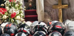 Kaski motocyklowe uczestników 18. Ogólnopolskiej Pielgrzymki Motocyklowej "Od Krzyża do Krzyża. Od Bałtyku do Tatr" ułożone w rzędach przed ołtarzem w kościele, obok kompozycji z kwiatów i złotego krzyża