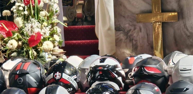 Kaski motocyklowe uczestników 18. Ogólnopolskiej Pielgrzymki Motocyklowej "Od Krzyża do Krzyża. Od Bałtyku do Tatr" ułożone w rzędach przed ołtarzem w kościele, obok kompozycji z kwiatów i złotego krzyża